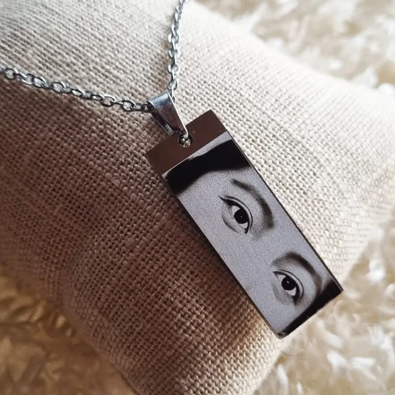 Dije rectangular plateado con fotograbado de ojos sobre cojín