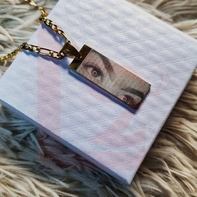 Dije rectangular dorado con fotograbado de una mirada sobre caja blanca