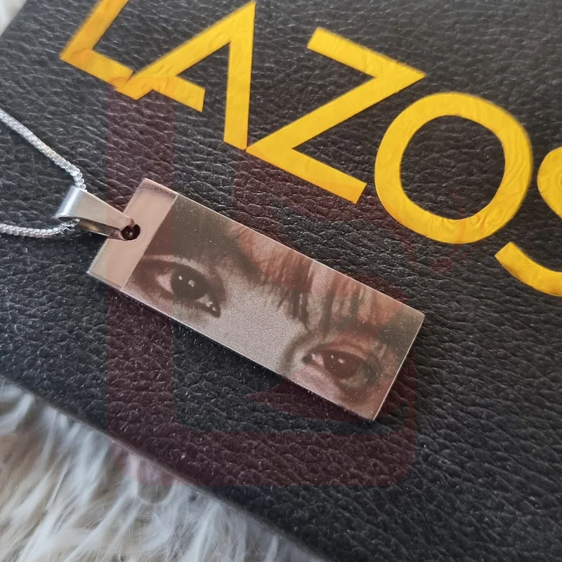 Dije rectangular plateado con fotograbado de ojos sobre empaque LAZOS